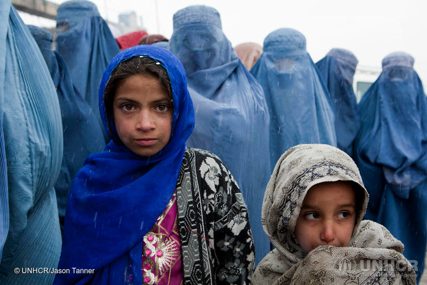 Afghanistan / Young girls wait in line with their mother at a UNHCR  distribution event at Tamir Mill Bus site. UNHCR distributes charcoal and NFI's to registered IDP's at one of Kabul's Informal Settlement Sites in the city centre. 57 families eek out a living in a dilapidated warehouse building owned by the Ministry of Transportation. The site originally served as a storage facility for the national bus company. Tajik and Pashtun families live side by side without any major conflict. Over 70% of the families are returnees from the period 2002-2004 who are unable to achieve sustainable reintegration in their places of origin and subsequently drifted to Kabul City in search of work. There is a nearby school which is accessible to the children but the poor economic circumstances of the many families oblige them to send their children out to work. low levels of literacy, particularly amongst the women, limit their access to employment other than the lowest paid daily wage labor. / UNHCR / J. Tanner / February 2011