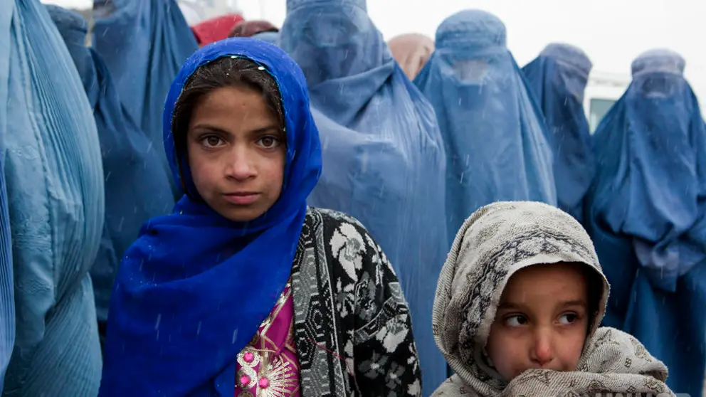 Afghanistan / Young girls wait in line with their mother at a UNHCR  distribution event at Tamir Mill Bus site. UNHCR distributes charcoal and NFI's to registered IDP's at one of Kabul's Informal Settlement Sites in the city centre. 57 families eek out a living in a dilapidated warehouse building owned by the Ministry of Transportation. The site originally served as a storage facility for the national bus company. Tajik and Pashtun families live side by side without any major conflict. Over 70% of the families are returnees from the period 2002-2004 who are unable to achieve sustainable reintegration in their places of origin and subsequently drifted to Kabul City in search of work. There is a nearby school which is accessible to the children but the poor economic circumstances of the many families oblige them to send their children out to work. low levels of literacy, particularly amongst the women, limit their access to employment other than the lowest paid daily wage labor. / UNHCR / J. Tanner / February 2011